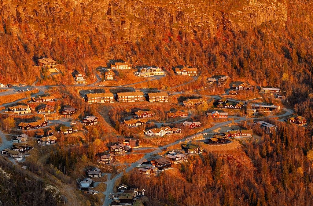 Telephoto aerial close-up of cabin complex among red rocks and forest in deep sunset light, Hemsedal Norway
